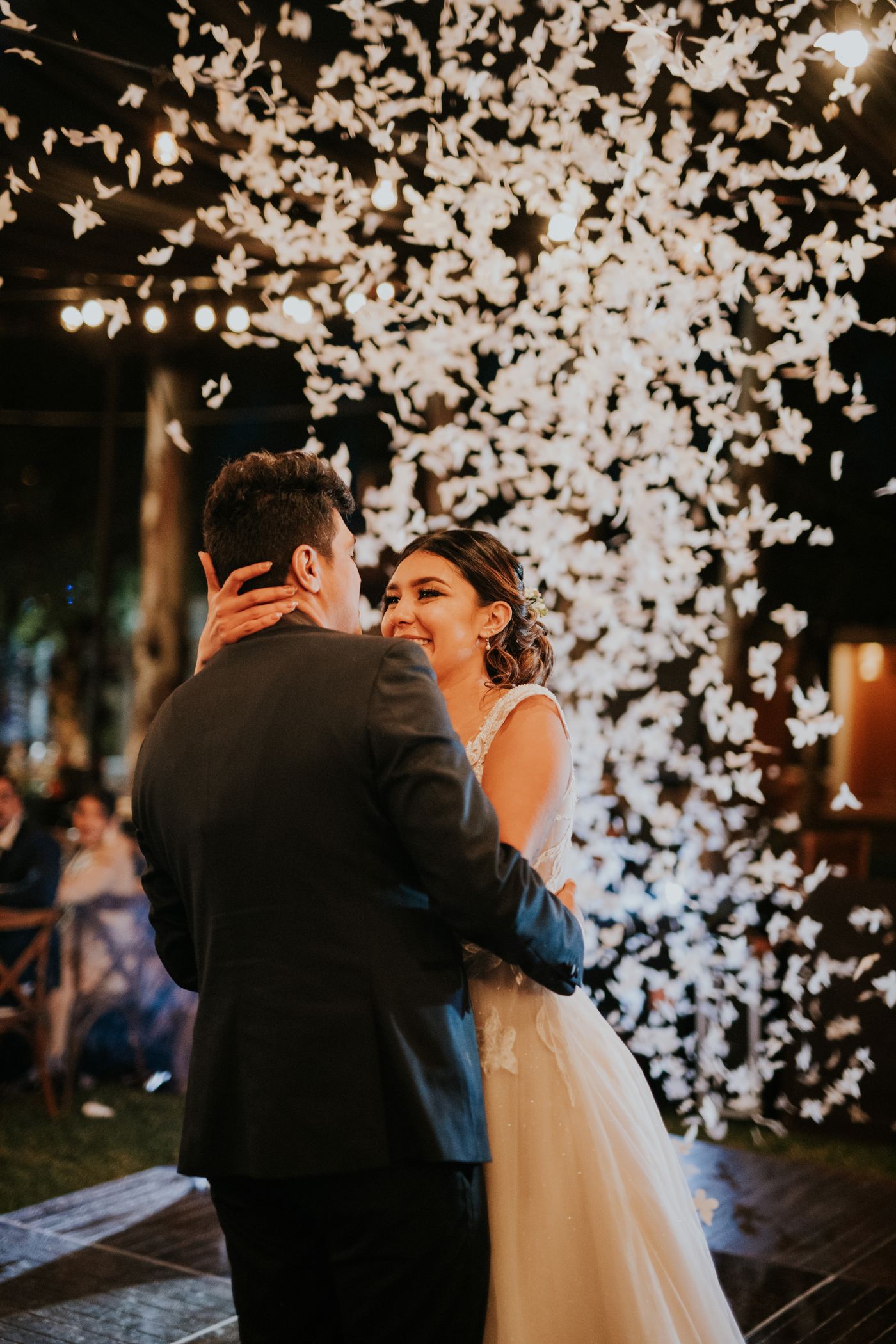 A couple dancing close as white confetti falls around them at night.