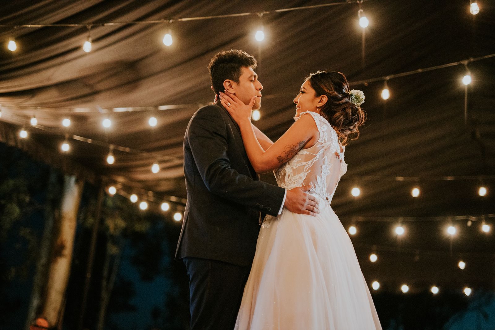 Bride and groom in a tender first dance beneath strings of warm lights.