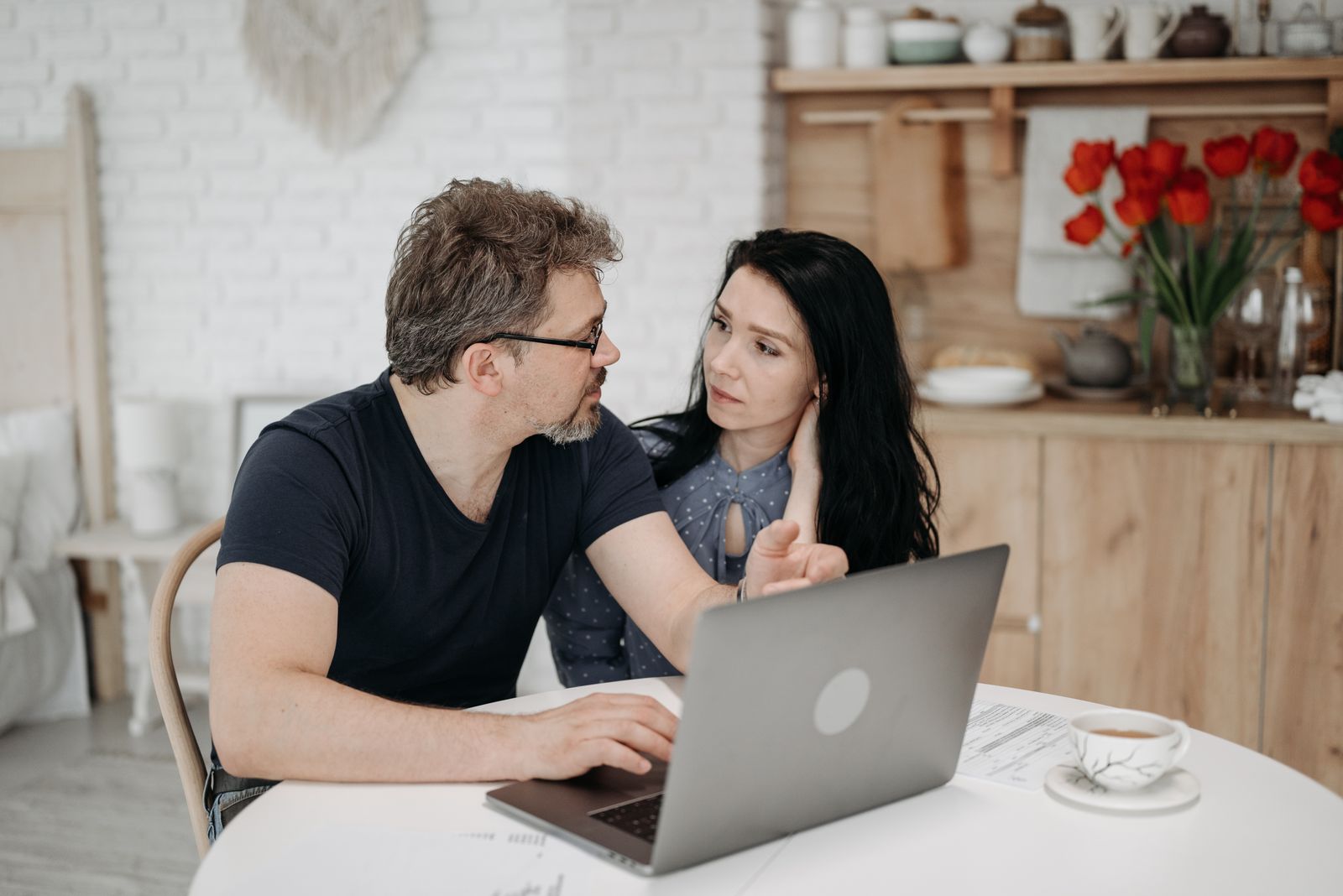 A couple at their kitchen table, planning together on a laptop.