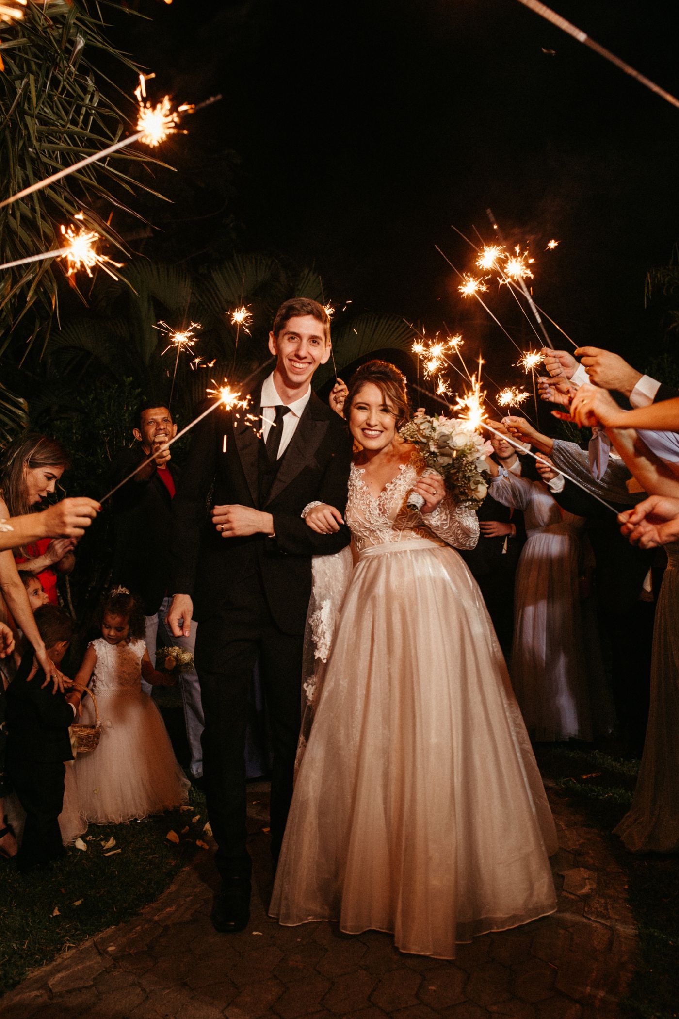 Newlyweds walking a path lined with guests holding sparklers at night.